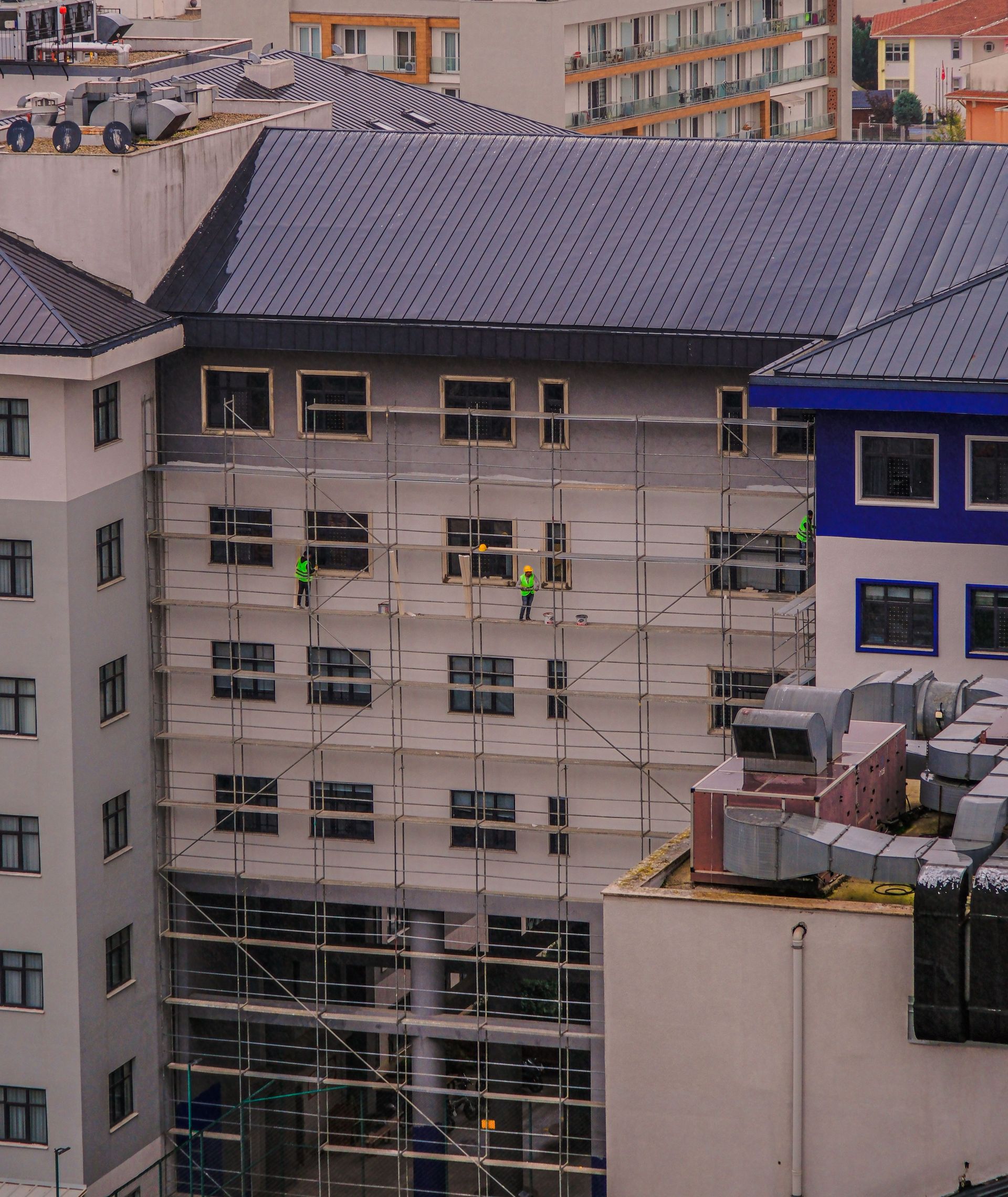 Scaffolding workers in bright vests maintain a building facade in Istanbul, Türkiye.